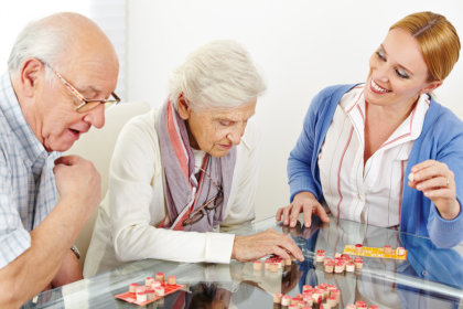 two elderly playing board games with their caregiver