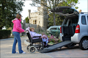 caregiver assisting an elderly woman sitting in a wheelchair to get inside a vehicle